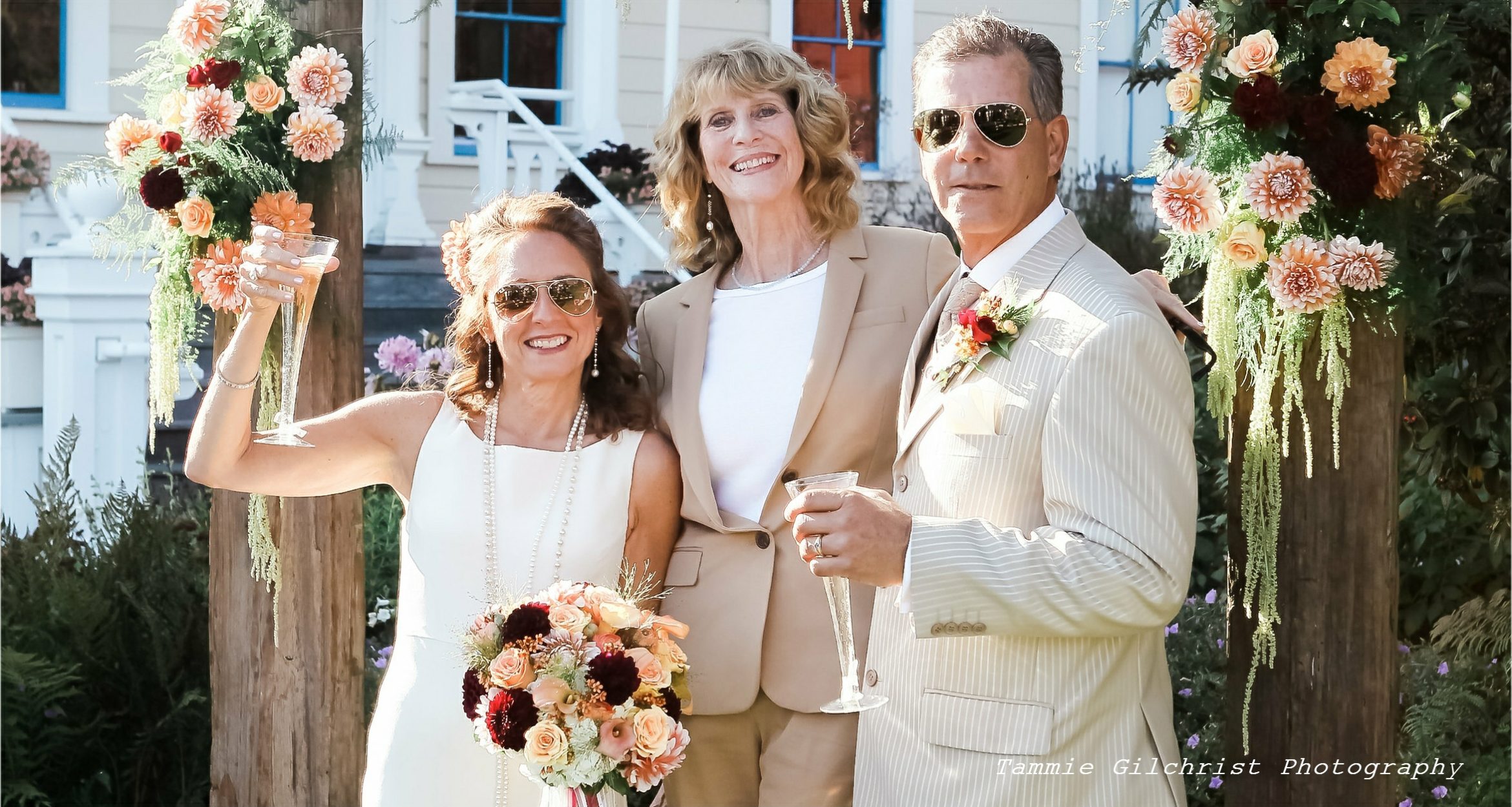 Suzanne and Ted raise flutes of champagne; Vanna Freeberg, proprietor and officiant of Elope Mendocino, drapes an arm over each of their shoulders.