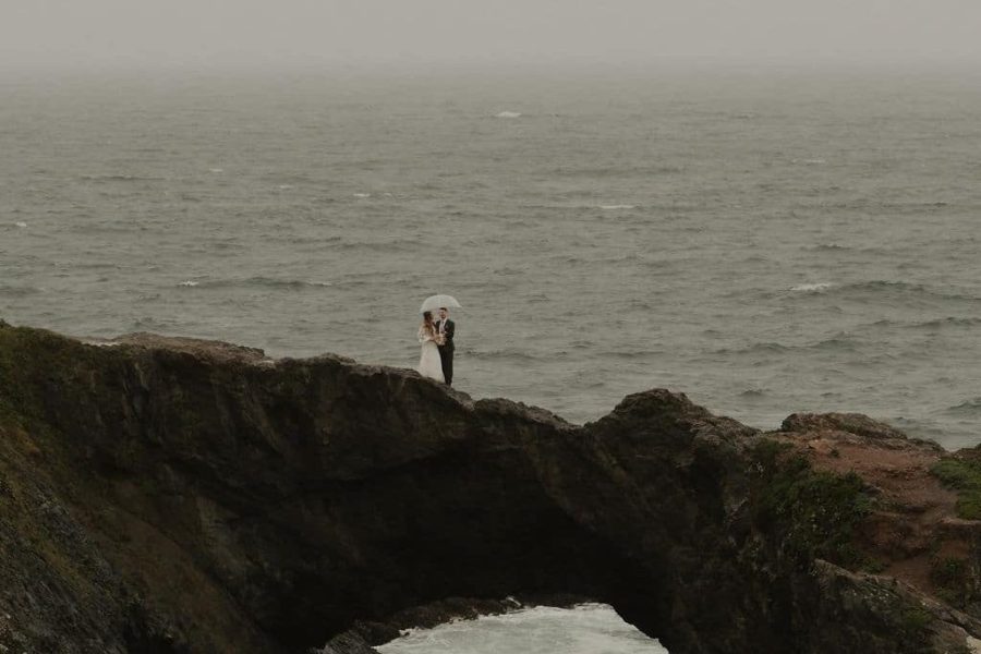 Couple with umbrella on coastal rock arch